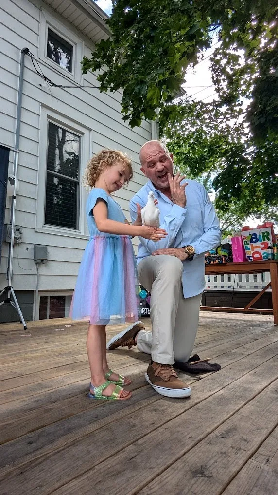 Little girl in blue dress holding white dove at backyard birthday party