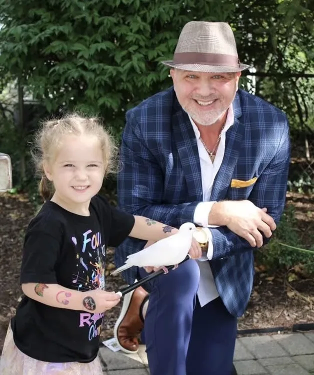 Mike DiDomenico with little girl holding white dove at outdoor birthday party